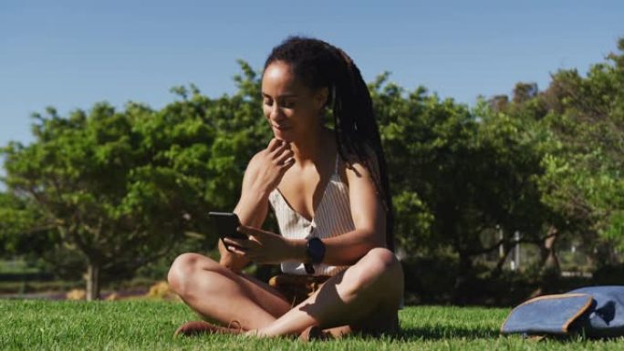 在公园里使用智能手机坐在草地上的非洲裔美国妇女