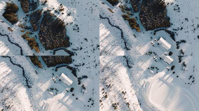 俯视图，在阳光明媚的早晨，无人机飞过田园诗般的冬季滑雪胜地乡村建筑和雪山景观。