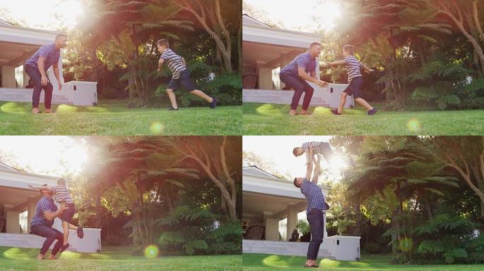 快乐的高加索儿子在阳光明媚的花园里奔跑并跳入父亲的怀抱