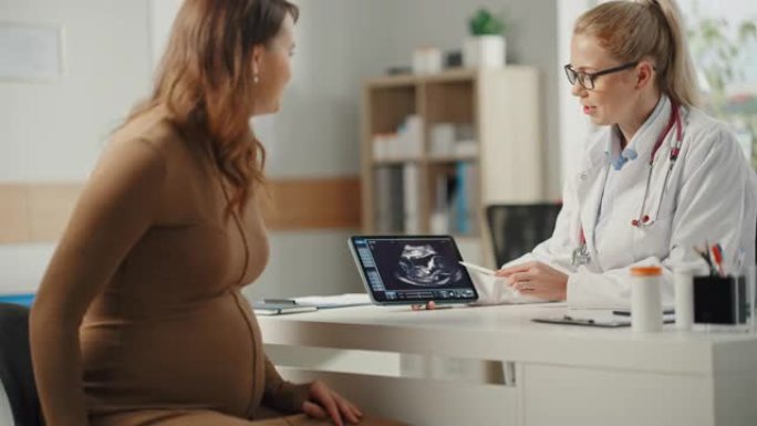 女医生在诊所咨询时向年轻的准妈妈展示平板电脑和超声妊娠扫描。坐在医院办公室桌子后面的家庭医生。