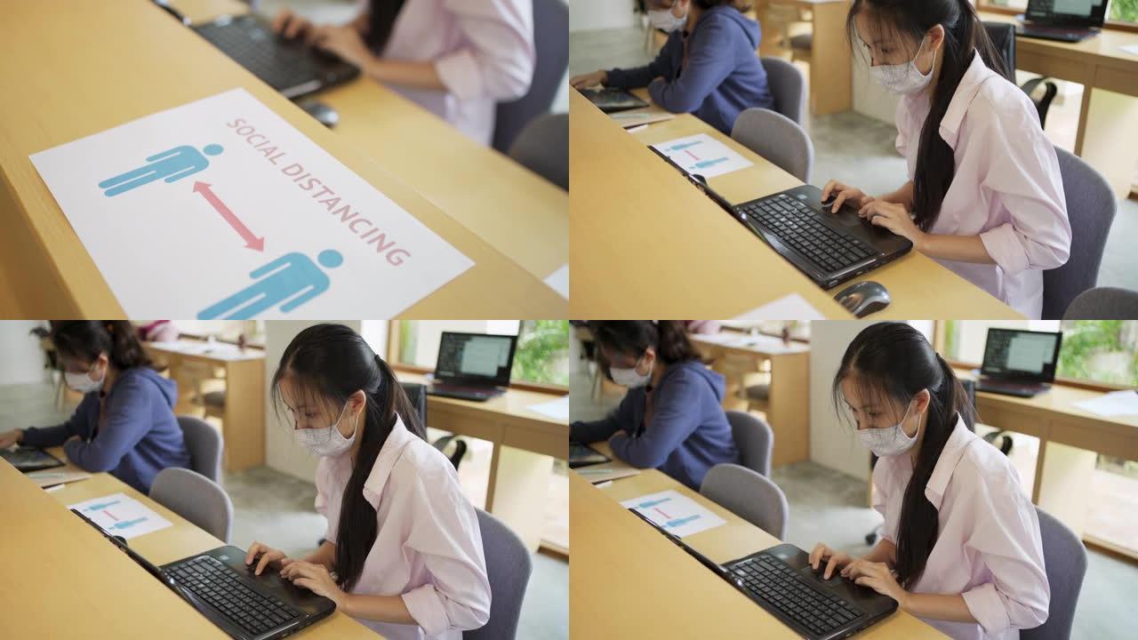 4k向上倾斜在共同工作空间办公室的桌子上拍摄社交距离标志，两名妇女在笔记本电脑上工作