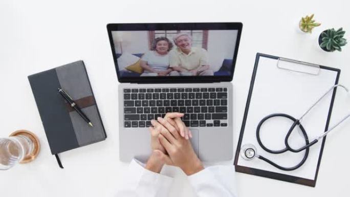 年轻的亚洲女医生在医疗制服和听诊器使用笔记本电脑通话视频电话会议在医疗诊所或医院的办公桌病人的俯视图