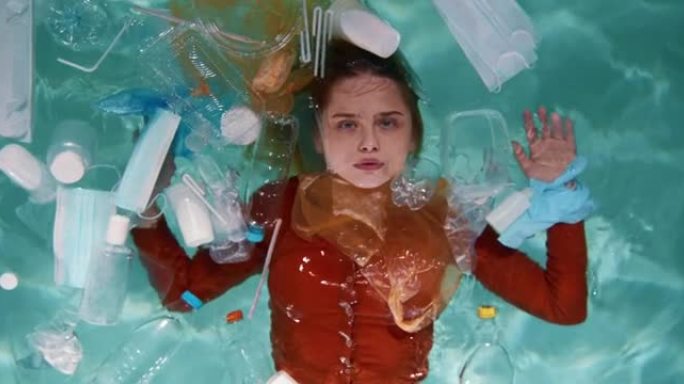 电影的俯视图，年轻漂亮的女人在水面上被一次性使用塑料包装的废物慢动作包围。