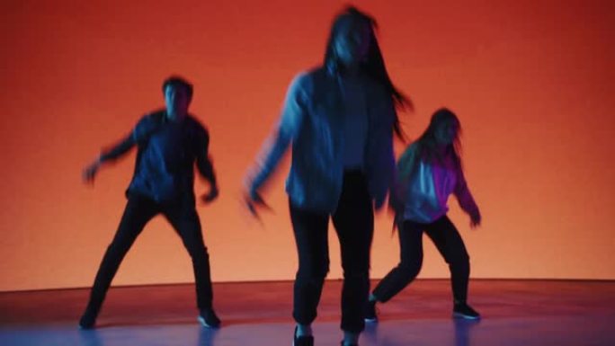 由三位时尚的专业舞者组成的多元化小组，在工作室环境中的虚拟制作过程中，在带有橙色背景的大Led墙屏幕