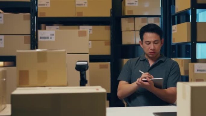 带有条码机和包装盒的亚洲商人在仓库快递之前，使用数字平板电脑检查货架上的库存和在线信息中的关键数据。