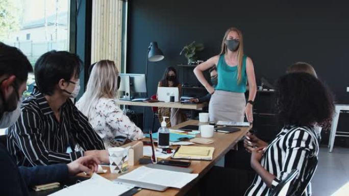 流感大流行期间的工作安全措施。年轻的白种商务女性领导着办公室会议，员工们戴着面具。