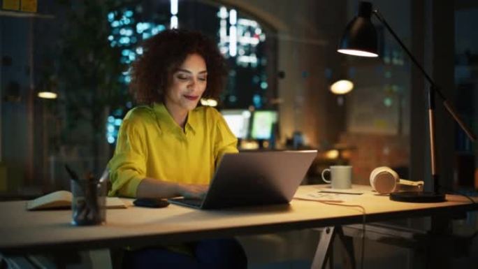 有动力的阿拉伯女性晚上坐在创意机构，经理为客户实施业务战略。兴奋的专家在笔记本电脑上编写公司项目计划