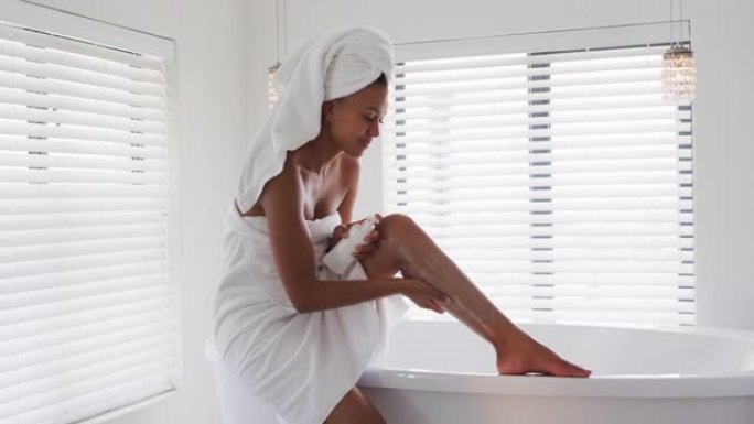 非裔美国妇女在家里的浴室在腿上涂抹保湿霜
