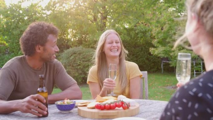 一群朋友坐在花园里的餐桌旁，用啤酒和香槟庆祝小吃