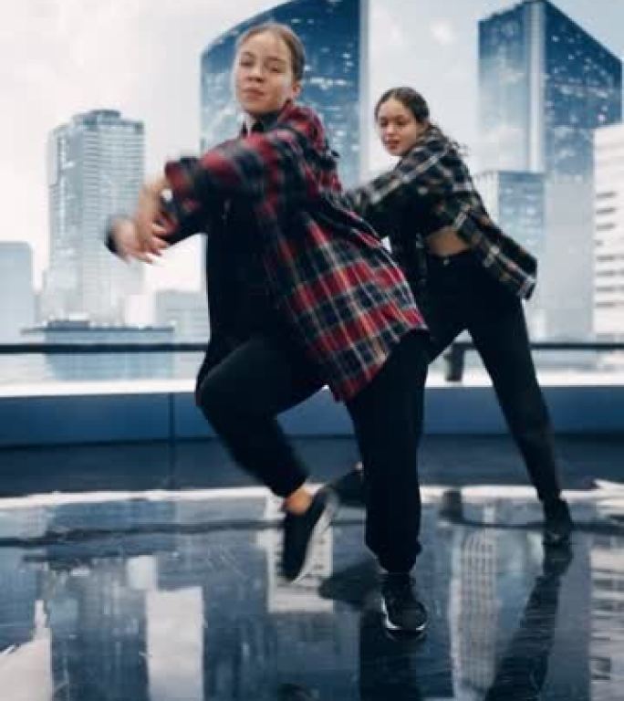 垂直屏幕: 两名时尚的年轻专业女舞者在大型Led墙壁屏幕前表演嘻哈舞蹈套路，现代城市天际线和工作室环