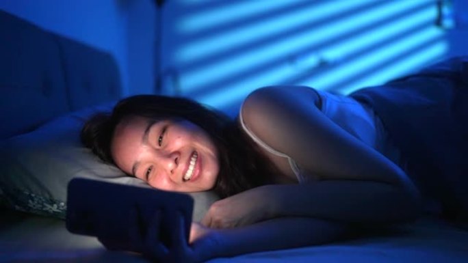亚洲妇女在床上用手机在家里传递信息