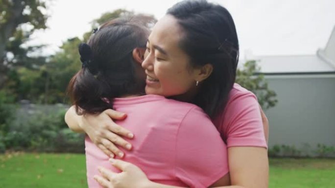 快乐的亚洲母亲和成年女儿在花园里拥抱和击掌，穿着粉色t恤