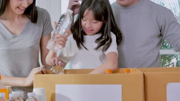 快乐的亚洲年轻家庭，教小女孩女儿关于可持续性的知识，如何打包免费的食物和饮料以运送到家里的捐赠箱中。