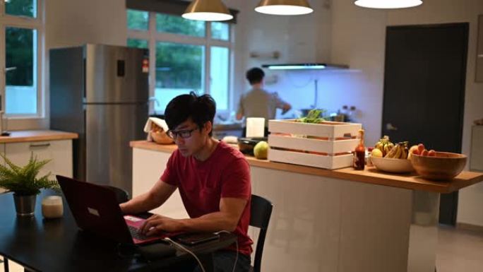 亚洲华人家庭在厨房准备早餐并使用笔记本电脑工作
