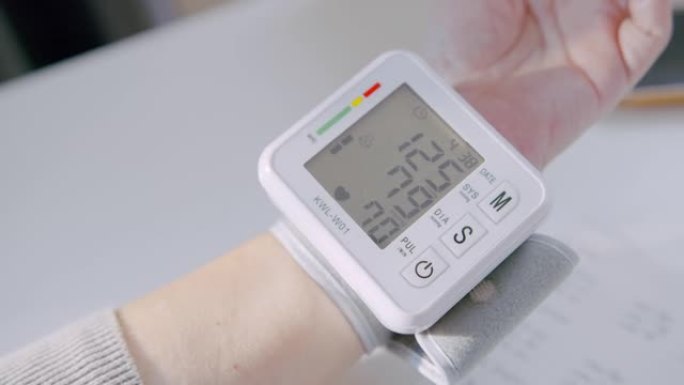 高级成人腕部监护仪检查血压在笔记本上记录她的血压数字