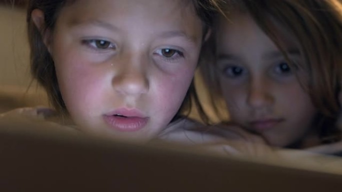 两个小女孩在黑暗中使用平板电脑或智能手机的电影特写镜头。概念: 网络技术的未来，视频技术，网络儿童的