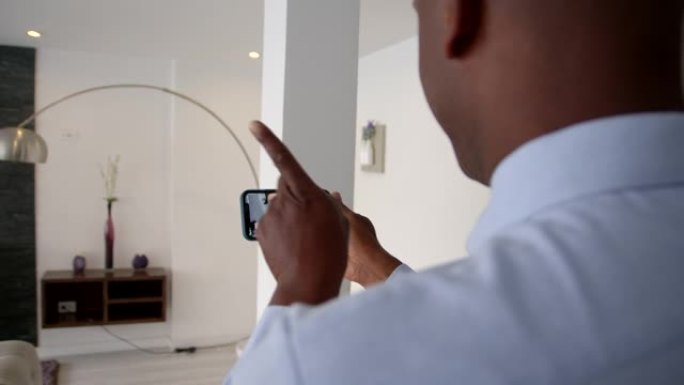 友好的黑人房地产经纪人使用智能手机为客户夫妇参观美丽的现代公寓