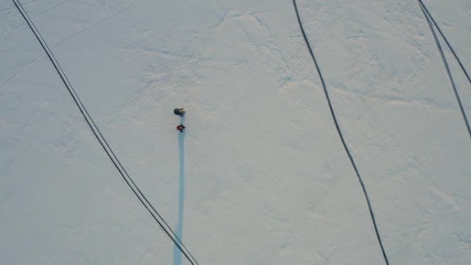 两个背着背包走过雪场的人的俯视图