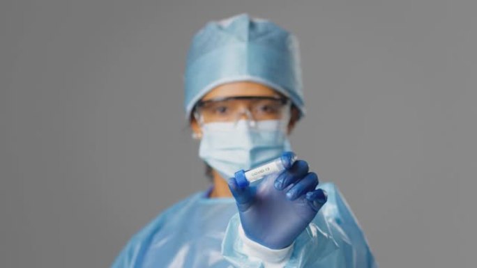 女性实验室研究人员戴着PPE拿着试管，标记为Covid 19