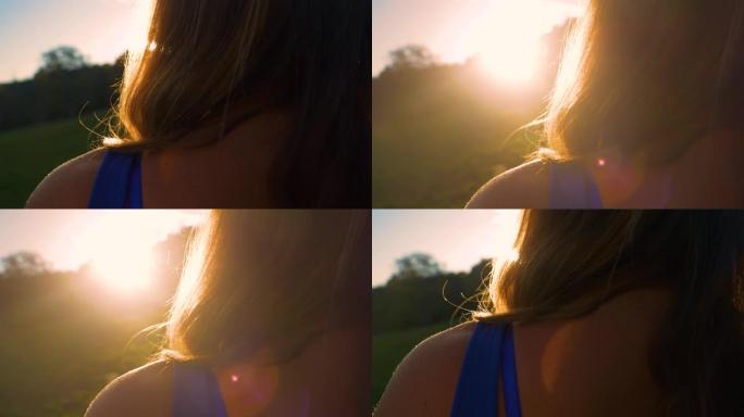特写镜头，镜头在看日落的漂亮年轻女士的肩膀上闪耀