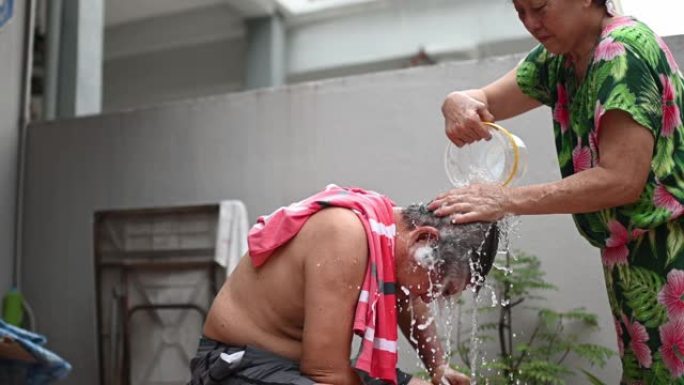 亚洲华裔高级妇女清洗丈夫的头发，在没有水的情况下在房子的前院洗头发