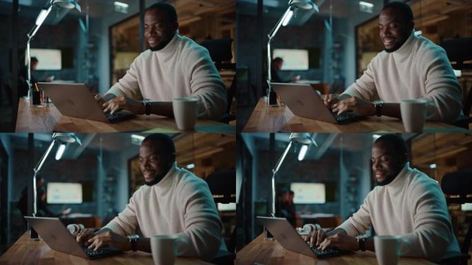 英俊的黑人非洲裔美国男子在创意办公环境中的笔记本电脑上进行在线对话。快乐男性正在浏览社交媒体，并在M