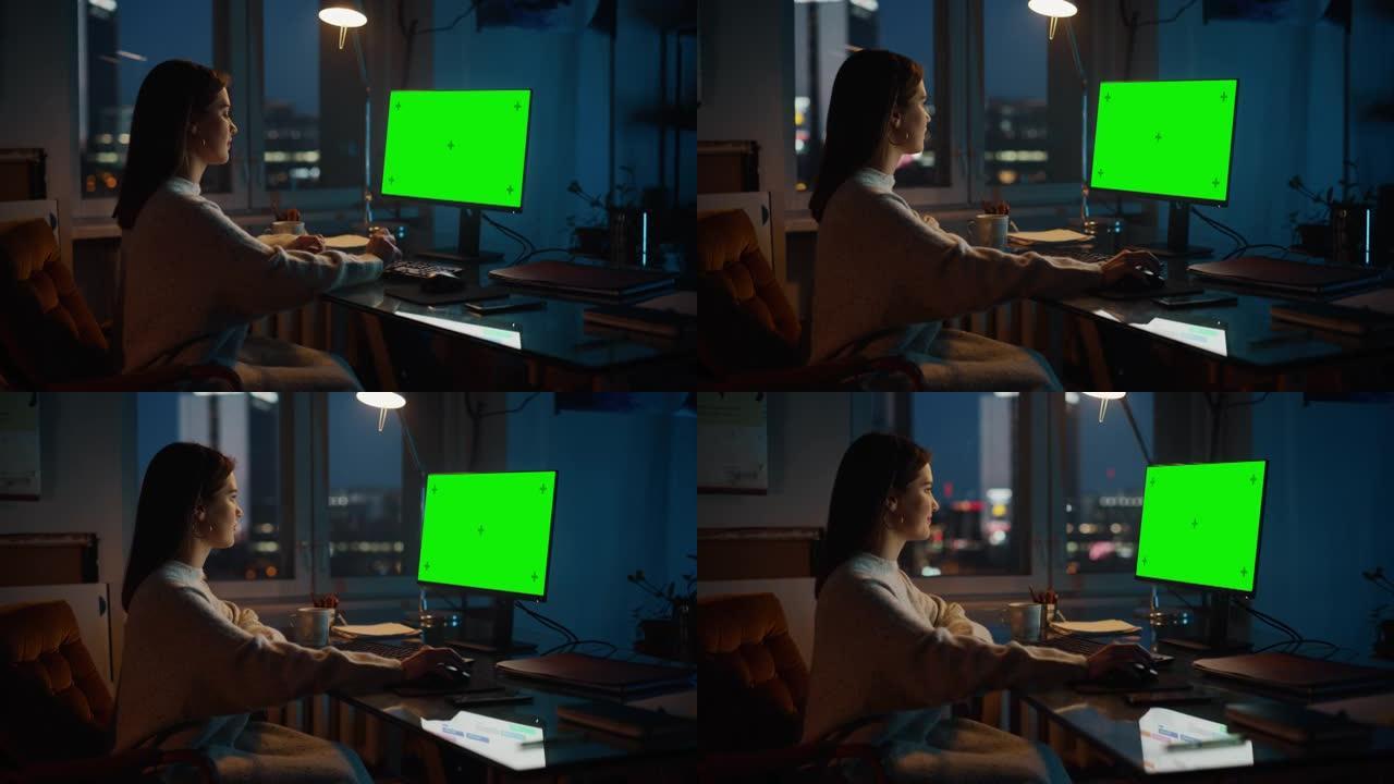 女经理在晚上设计时尚的黑暗阁楼办公室的创意机构中，在带有绿屏Chromakey模型的台式计算机上工作