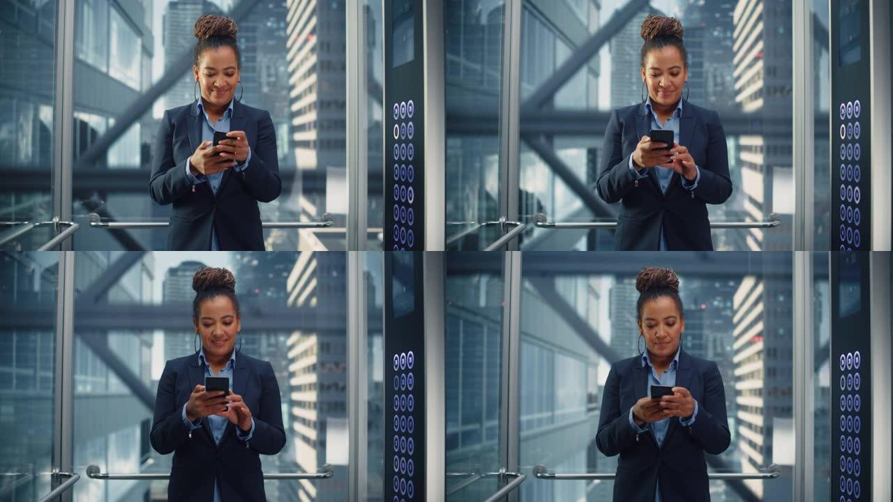 自信的黑人成年女性乘坐玻璃电梯到现代商务中心的办公室。成功的非洲裔美国经理使用智能手机，在电梯里写信