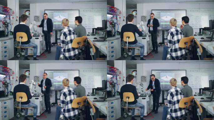 男老师展示了机器人手臂的细节，并与大学机器人课的学生进行了头脑风暴。坐在大学的年轻工程师群体多样。计
