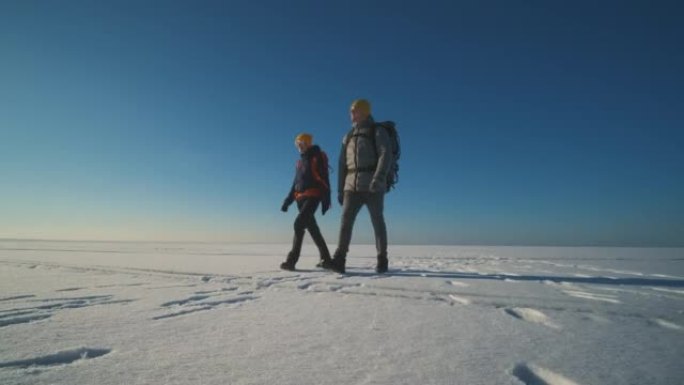 两个背着背包的游客走过雪场。慢动作