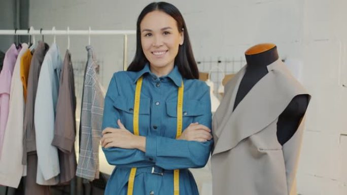 亚洲年轻女性裁缝站在新衣服背景下的陈列室里