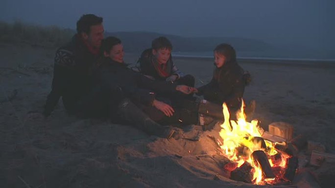 家人坐在冬天的海滩上着火