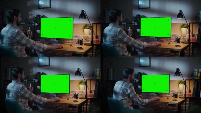 年轻英俊的男人在家工作，在带有绿屏模拟显示的台式计算机上。创意男性查看社交媒体，浏览互联网。晚上阁楼