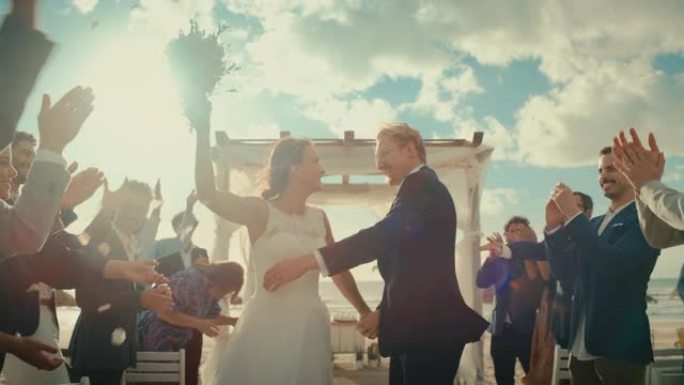 美丽的新娘和新郎在海边的海滩上户外庆祝婚礼。完美的婚姻场所，最好的多民族多元朋友向新婚夫妇投掷花瓣。