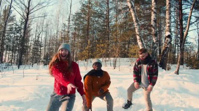 三个兴奋有趣快乐的多民族朋友在阳光明媚的冬季森林慢动作中向相机扔雪球很开心。