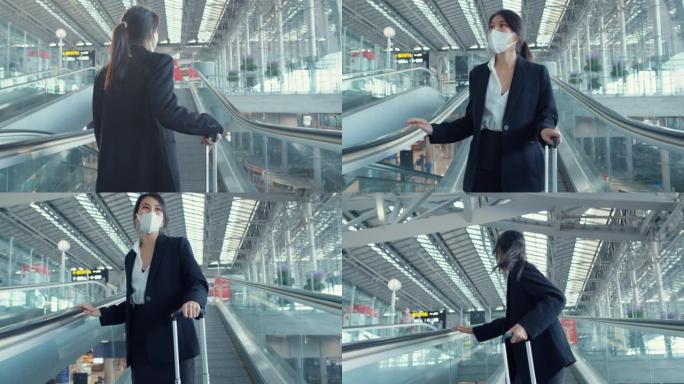 亚洲女商人戴着口罩在自动扶梯上拖着行李架环顾四周，走到国际机场航站楼。