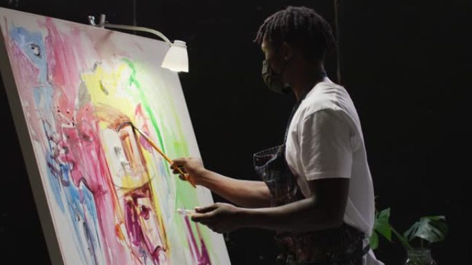 非裔美国男性艺术家在艺术工作室的画布上戴着口罩绘画