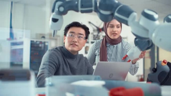 亚洲工程师与机器人开发实验室的中东女同事重新定位和检查机械臂。机器人机构的设计、操作和性能研究