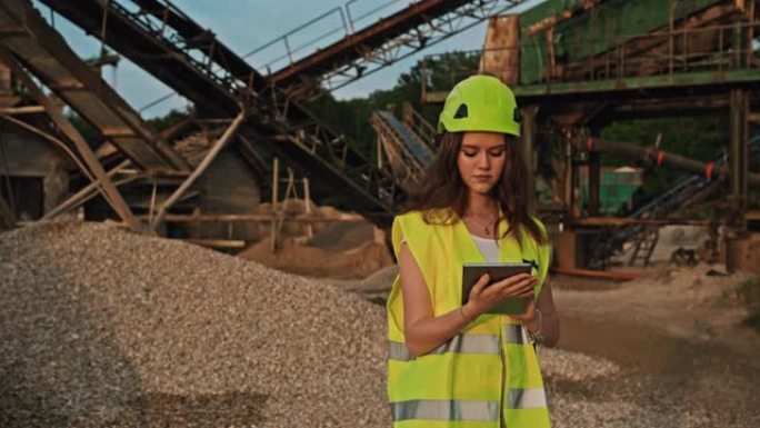手持慢动作拍摄黑发女采矿工程师使用平板电脑，采矿坑充满挖掘机器背景