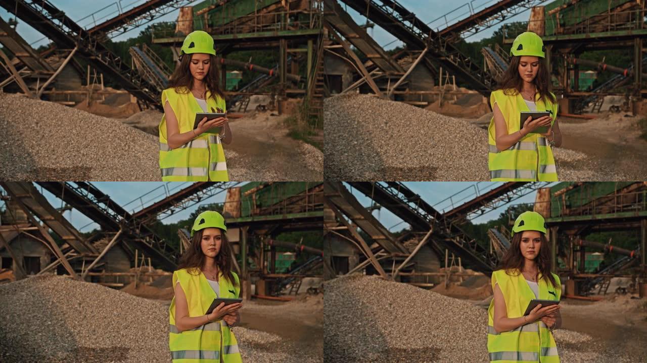 手持慢动作拍摄黑发女采矿工程师使用平板电脑，采矿坑充满挖掘机器背景