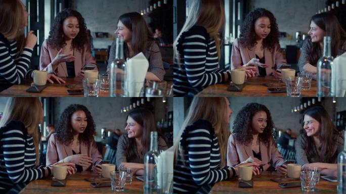 友谊概念。三个年轻快乐美丽的多民族女性朋友在时髦的餐厅餐桌上随意交谈。