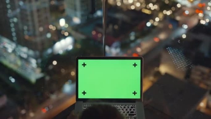 晚上在屋顶露台上使用色度键绿屏笔记本电脑的女人