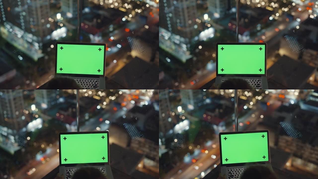 晚上在屋顶露台上使用色度键绿屏笔记本电脑的女人