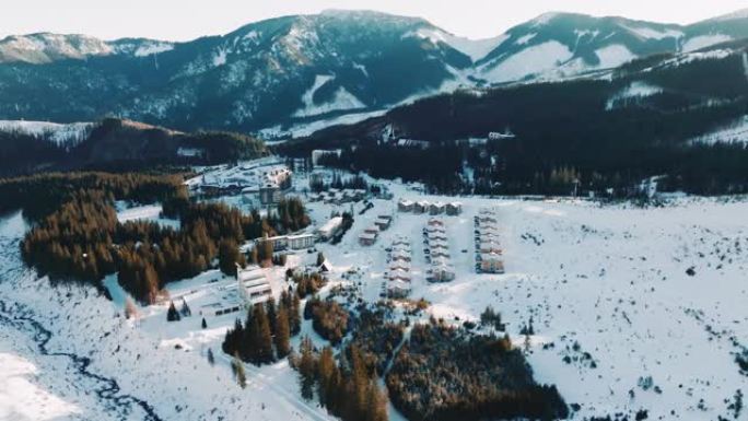 在阳光明媚的早晨雪山景观中，田园诗般的冬季滑雪胜地乡村建筑的长全景空中拍摄。