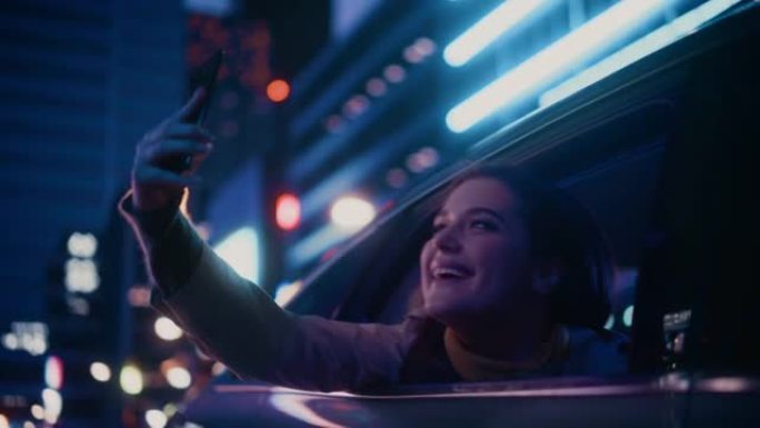 晚上，兴奋的女性从汽车后座望向窗外。女人在智能手机上拍照和录像，惊讶地发现带有工作霓虹灯的城市街道多