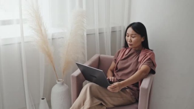 亚洲女性在扶手椅上使用笔记本电脑