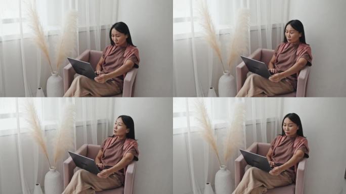 亚洲女性在扶手椅上使用笔记本电脑