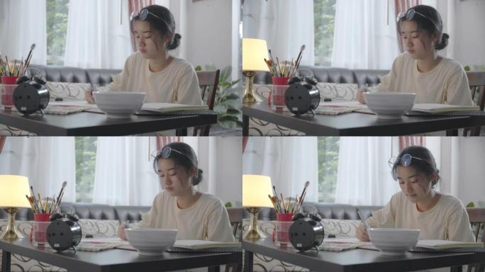 亚洲少女使用笔记本电脑进行视频通话，在家与朋友交谈和微笑，同时画水彩画。她在vlog社交媒体上使用视