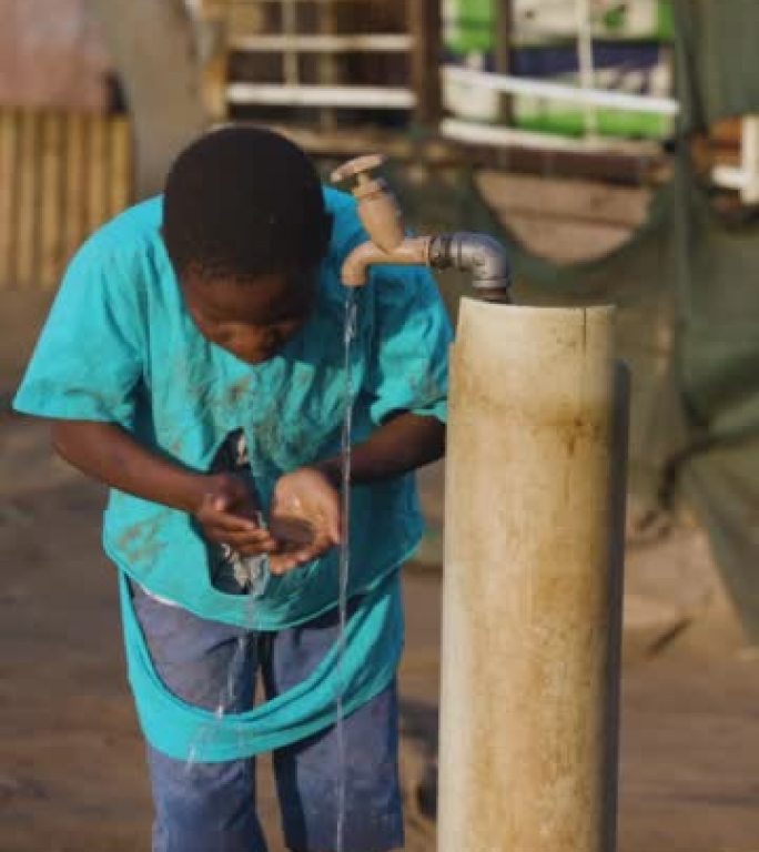 垂直视频。贫穷。不平等。年轻的非洲黑人男孩从公共水龙头喝水