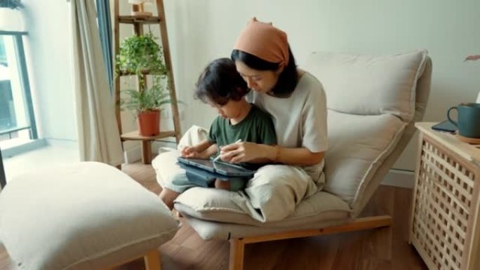 可爱的亚洲妈妈在平板电脑上帮助儿子做作业。